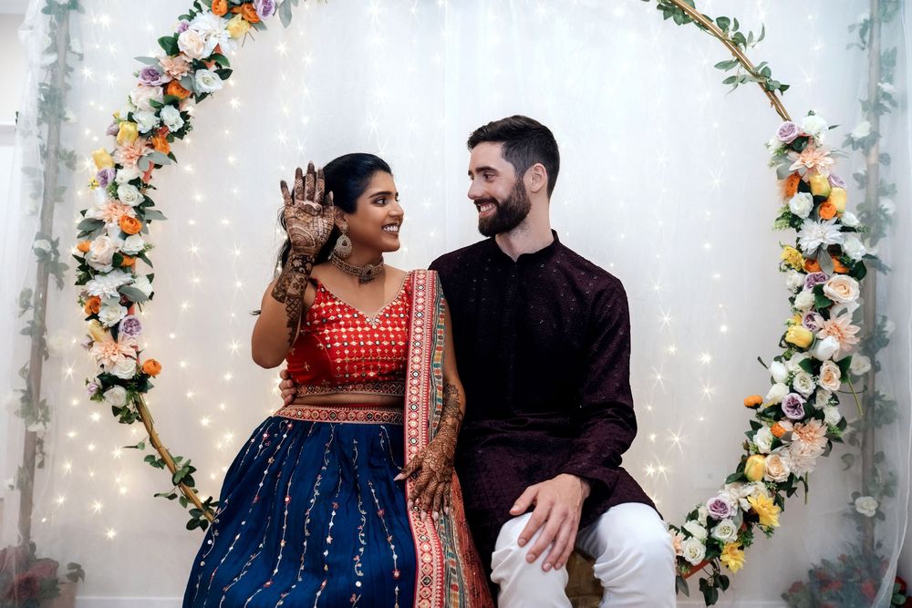 Cultural wedding celebration under floral arch with string lights and decorative backdrop.