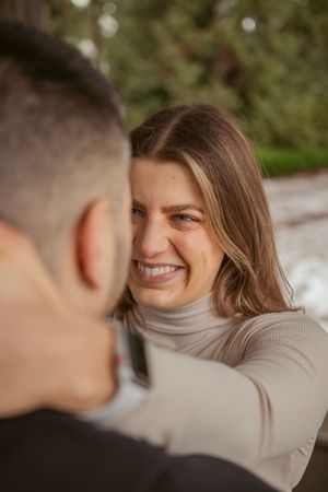 A romantic couple sharing joyful moments while sitting outdoors, with one wearing a light beige turtleneck sweater.