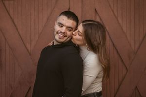 A loving couple embracing against a rustic barn door background in warm lighting.