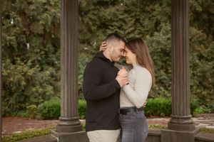 A romantic couple sharing an intimate moment between decorative stone pillars in a garden.