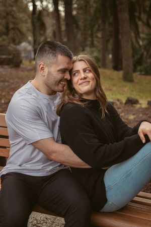 A couple relaxing together on a wooden bench in a forest setting during autumn.