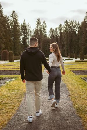 A couple walking along a scenic garden path surrounded by tall pine trees.