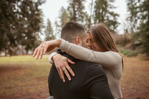 A couple embraces in an intimate moment outdoors with tall evergreen trees in the background on an autumn day.