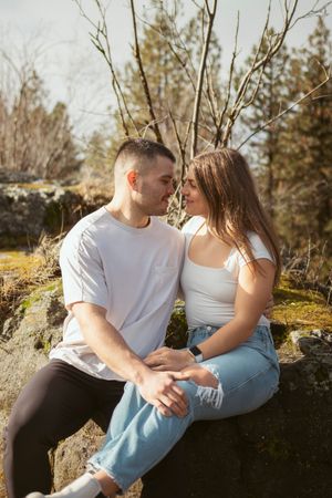A couple sharing an intimate moment while sitting on mossy rocks outdoors.