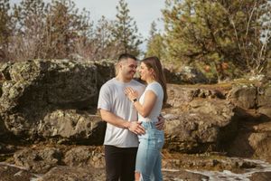 Couple embracing near rocky coastal formations during a sunny outdoor photoshoot.