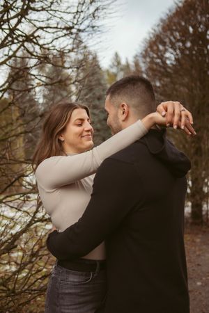 A romantic embrace between a couple standing in a wooded area during autumn.