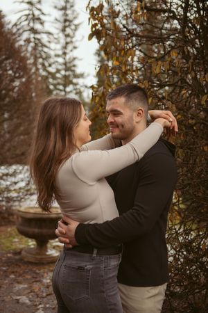 A couple embracing and smiling at each other in an outdoor garden setting during autumn.