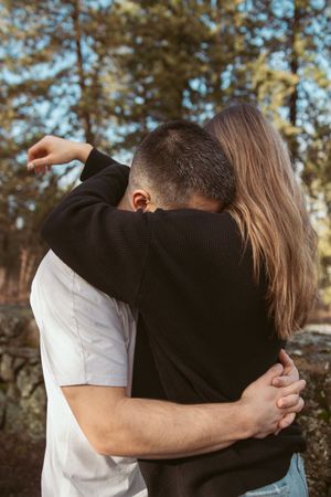 A romantic couple sharing an intimate embrace outdoors in a sunlit forest setting.
