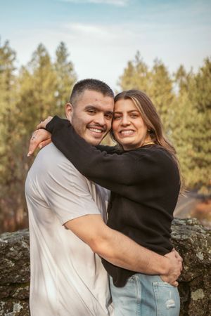 Couple embracing and smiling while standing on rocky outcrop with evergreen forest backdrop.