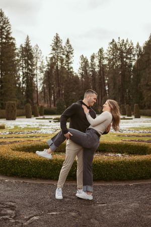 A playful sequence of a couple performing a romantic dip pose in a park with pine trees.