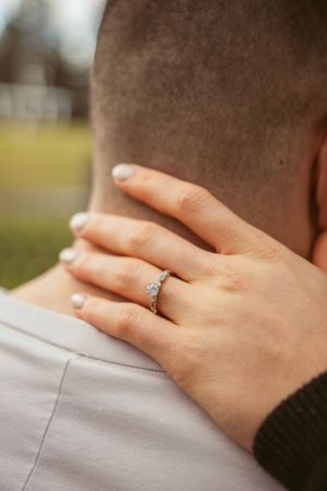 A close-up shot of a delicate engagement ring on a hand resting on a shoulder.
