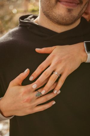 Close-up of hands showing engagement ring against black sweater background.