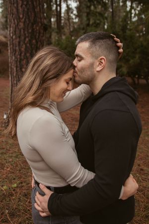 Romantic couple embraces in a pine forest during autumn with warm earth tones in the background.