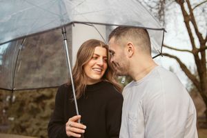 A couple sharing intimate moments under an umbrella on an overcast day.