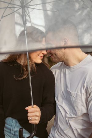 Couple sharing a romantic moment under a clear umbrella with sunlight filtering through on a cloudy day.
