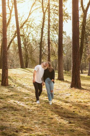 Couple walking through a sunlit forest with tall pine trees on an autumn afternoon with golden light filtering through.
