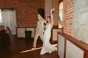 A playful dance moment between a couple in a rustic brick venue with natural light streaming through windows.