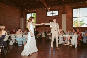 Wedding guests watch as dancing occurs on the hardwood floor of an industrial-style venue with exposed brick walls.