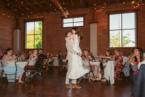 Wedding couple sharing a romantic dance lift in a rustic venue surrounded by guests.