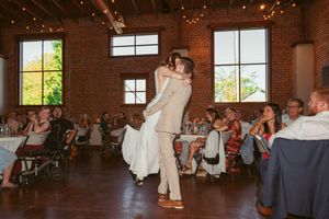 Dancing couple perform a romantic twirl in front of wedding guests at a rustic brick-walled reception venue.