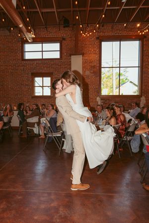A romantic dance moment during a wedding reception in an industrial brick-walled venue with string lights.