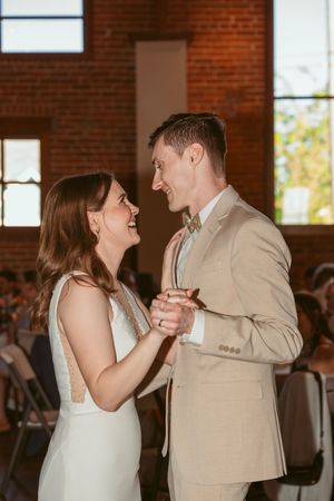 Couple shares a romantic dance moment in a brick-walled venue with natural light streaming through windows.