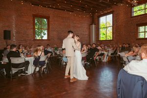 Reception venue features exposed brick walls, string lights, and guests enjoying dance performances.