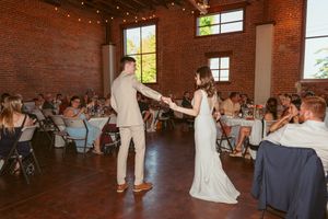 Couple performing first dance in an industrial-style venue with exposed brick walls and twinkle lights.