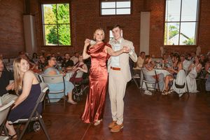 Couple dances together during wedding reception in industrial brick venue with string lights overhead.