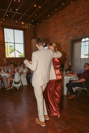 A couple shares their first dance in a rustic brick venue decorated with string lights overhead.