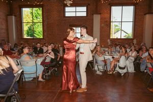 A couple performs a dance in a sunlit brick venue while guests in folding chairs watch from the sides.