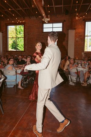 Dancing partners move across the hardwood floor at a wedding reception while guests watch from their seats.