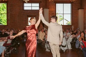 Wedding guests dance energetically in a rustic brick venue with large windows and string lights.