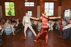 Dancers spin and twirl on the dance floor at a reception in an industrial brick venue with natural lighting.