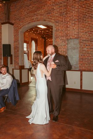 Couple sharing an intimate slow dance in a rustic brick-walled venue with string lights overhead.