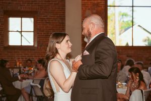 A couple performs an energetic dance move in a rustic brick venue with string lights overhead.
