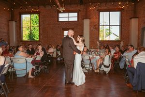 Couple dances energetically in a rustic brick venue with string lights overhead and guests watching from tables.