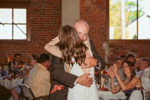 A couple shares their first dance at a wedding reception in a rustic brick venue with string lights overhead.