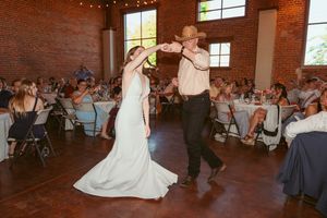 A couple performs their first dance in an elegant brick-walled venue surrounded by seated wedding guests.