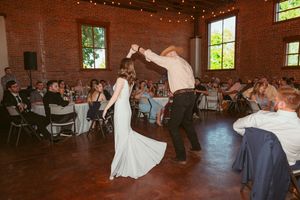 Wedding guests watch as dancers twirl across a hardwood floor in an industrial-style reception venue.