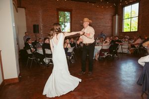 A beautiful father daughter dance in a rustic brick venue with string lights overhead.
