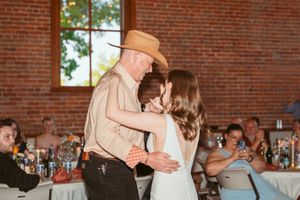 A special dance moment unfolds at a rustic wedding reception as guests observe from their tables.