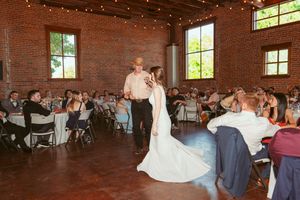 Wedding couple dancing and celebrating with guests in a rustic brick venue with string lights overhead.