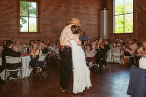 A couple dances together in an elegant brick-walled venue while wedding guests watch from dining tables.