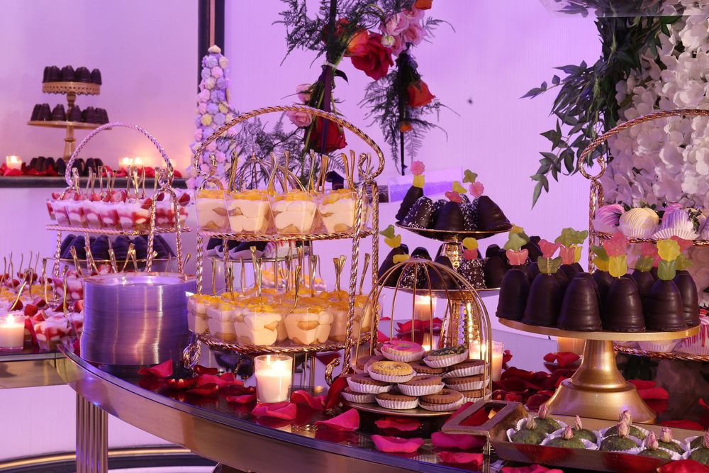 Luxurious wedding banquet setup featuring ornate floral centerpieces and golden decor bathed in purple atmospheric lighting.