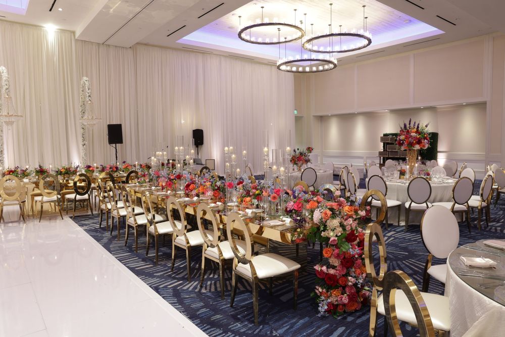 Elegant ballroom setup with round tables, white chairs, crystal chandeliers and floral centerpieces for a formal event.