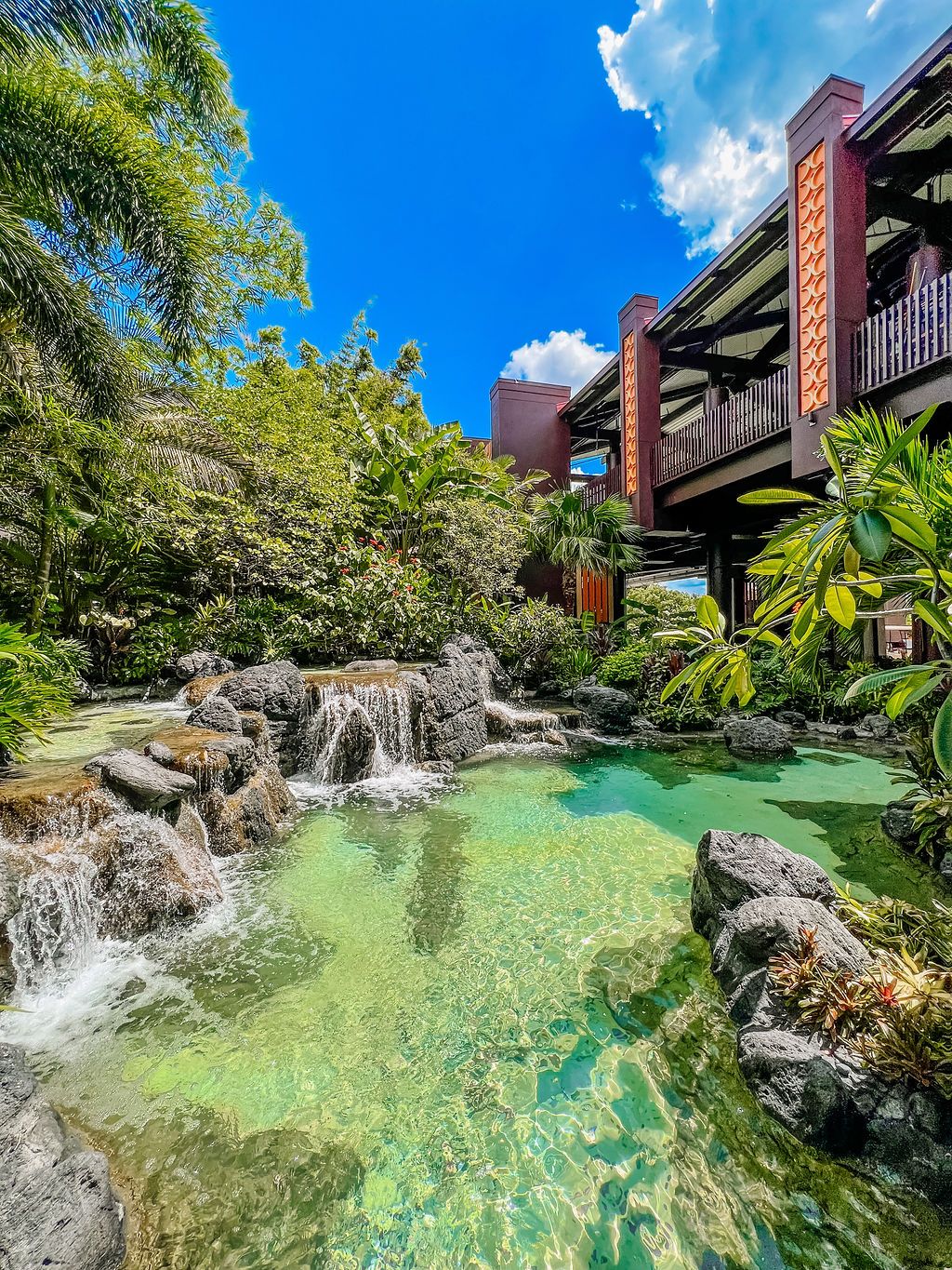 Tropical landscape with cascading waterfalls and turquoise pool at a luxury resort.