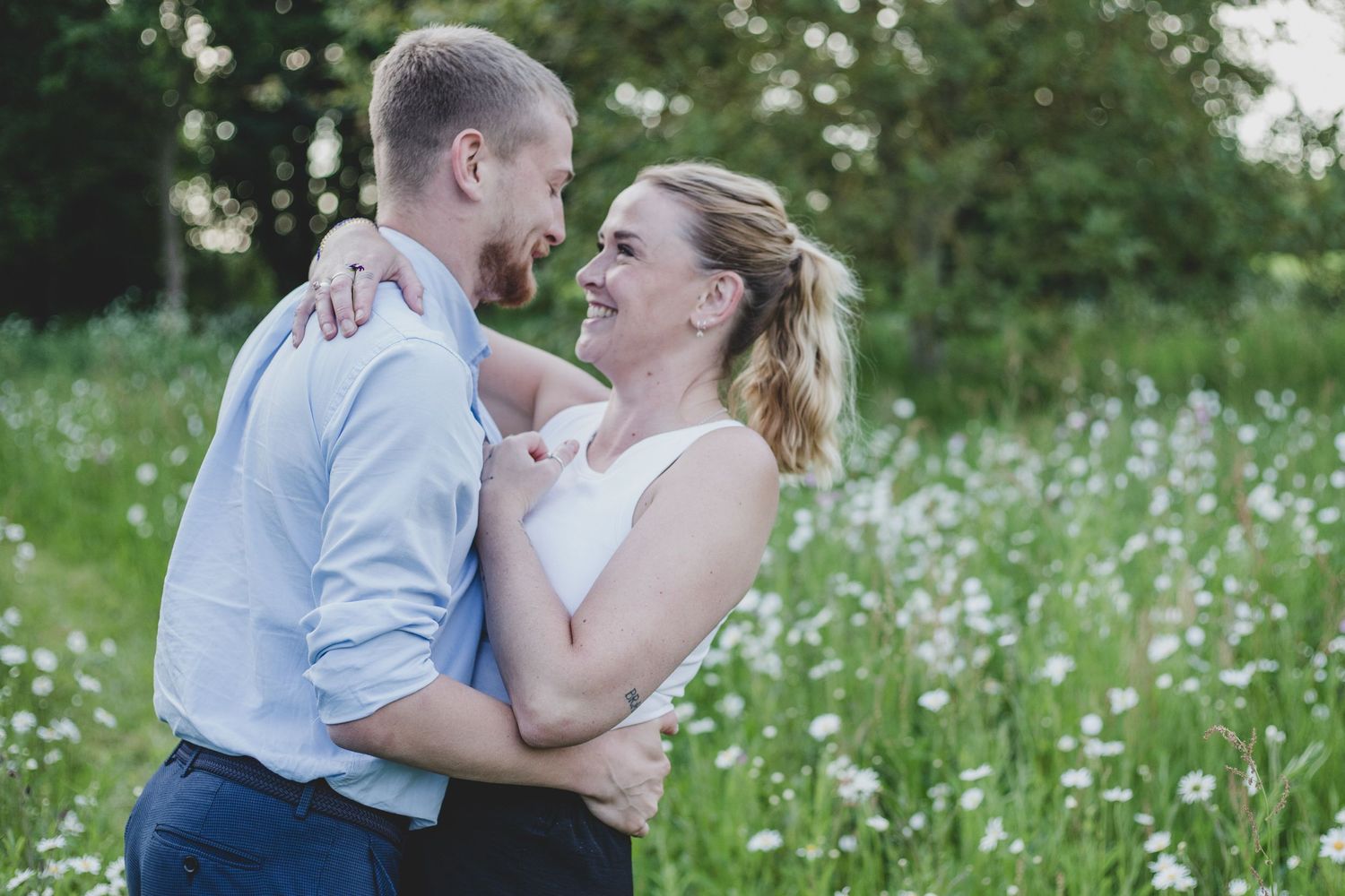 Loving couple embraces in a blooming meadow filled with wildflowers and lush grass on a sunny day.