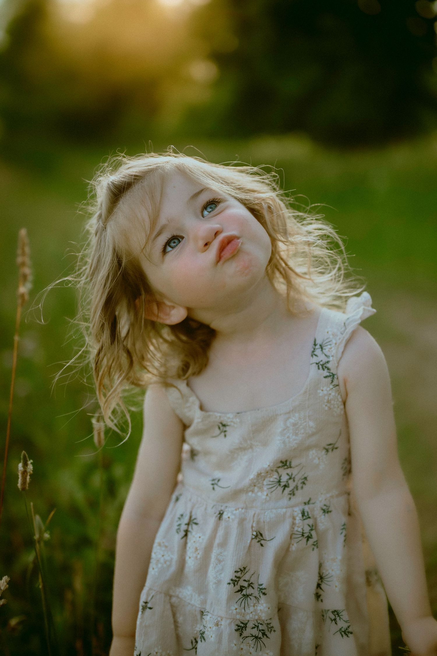 A child in a white floral dress tilts their head at various angles in a dreamy outdoor photoshoot at golden hour.