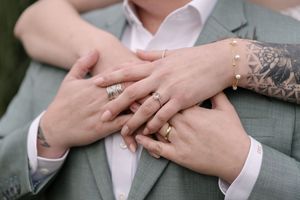 Close-up series of hands exchanging wedding rings during a ceremony as fingers interlock against grey attire.